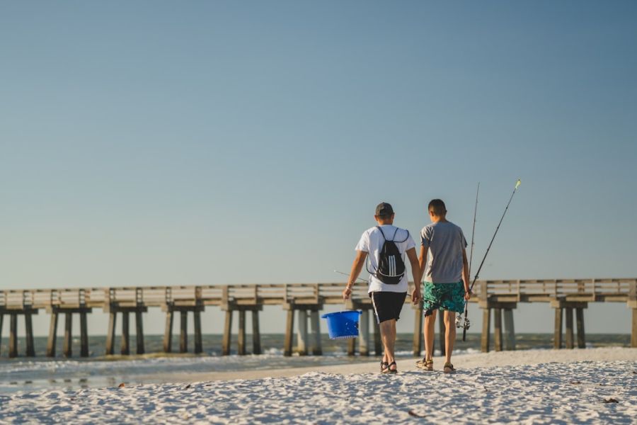 Two men walk along beach with fishing gear