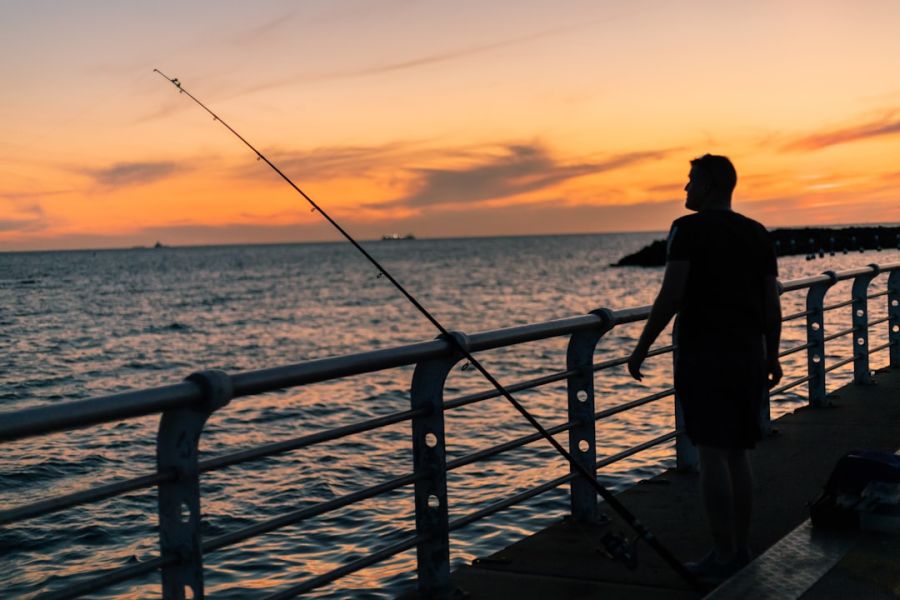 Man fishing on pier at sunset.