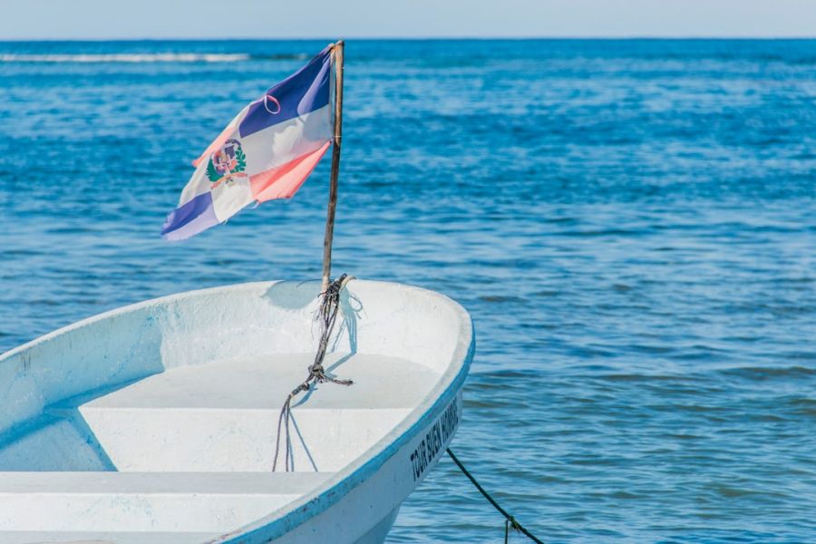 Small white boat with Dominican flag on water.
