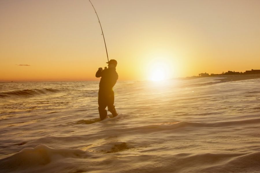 Silhouette fisherman casting rod at sunset beach