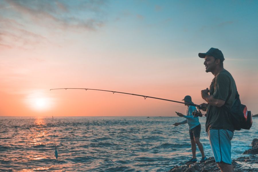 Two men fishing at sunset on rocky shore