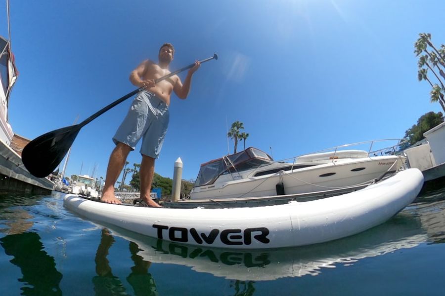 Shirtless man paddleboarding near boats.